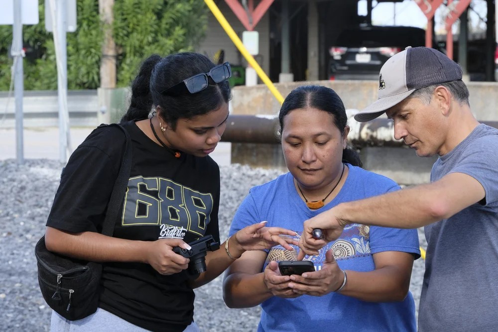 Three club members reviewing something on a phone together near the water
