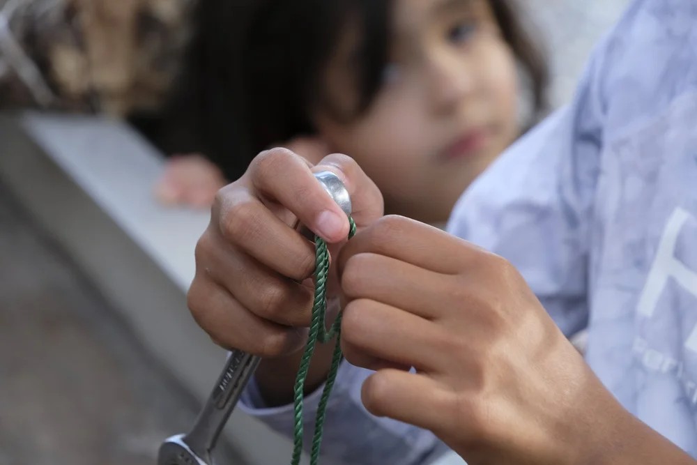 Close-up of a child's hands tying a fishing knot using a crimping needle