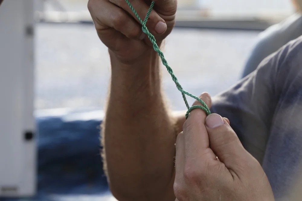 Instructor's hands demonstrating a fishing knot technique with green line