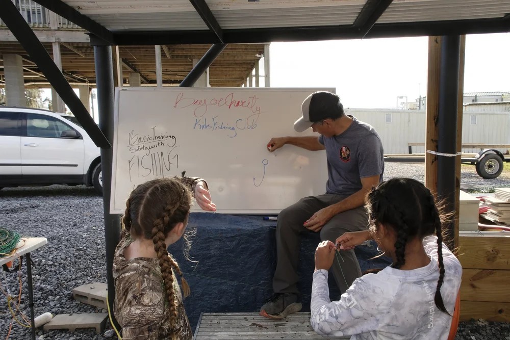 Instructor teaching two girls fishing knots at the Kids Fishing Club whiteboard session