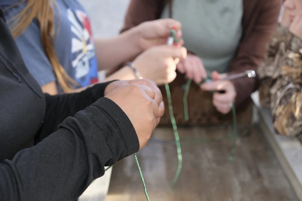 Multiple participants practicing fishing knots with green line at a workbench