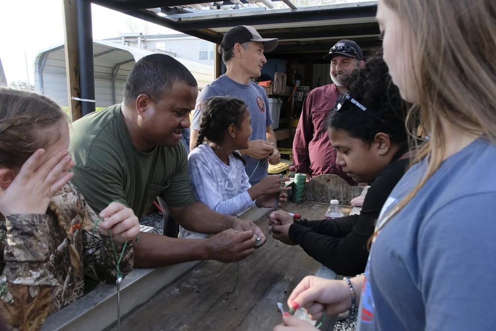 Families and volunteers practicing fishing knots together at an outdoor workshop table
