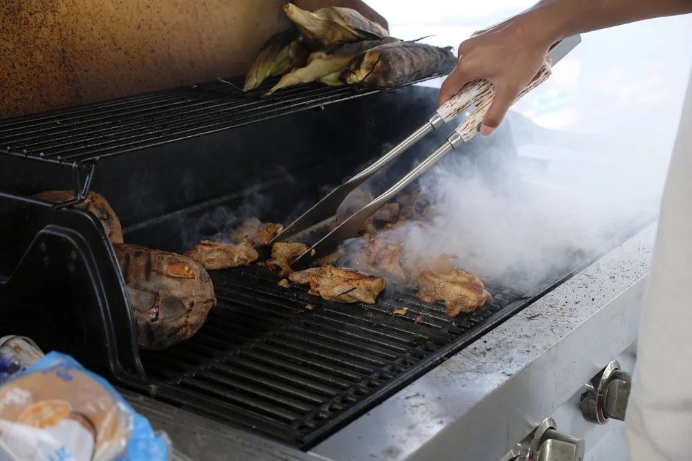 Close-up of chicken and vegetables being grilled with tongs at a club gathering