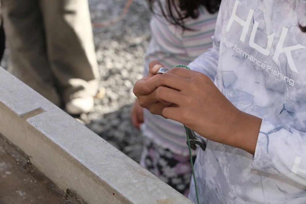 Child in HUK Performance Fishing shirt learning to tie a knot with a crimping tool