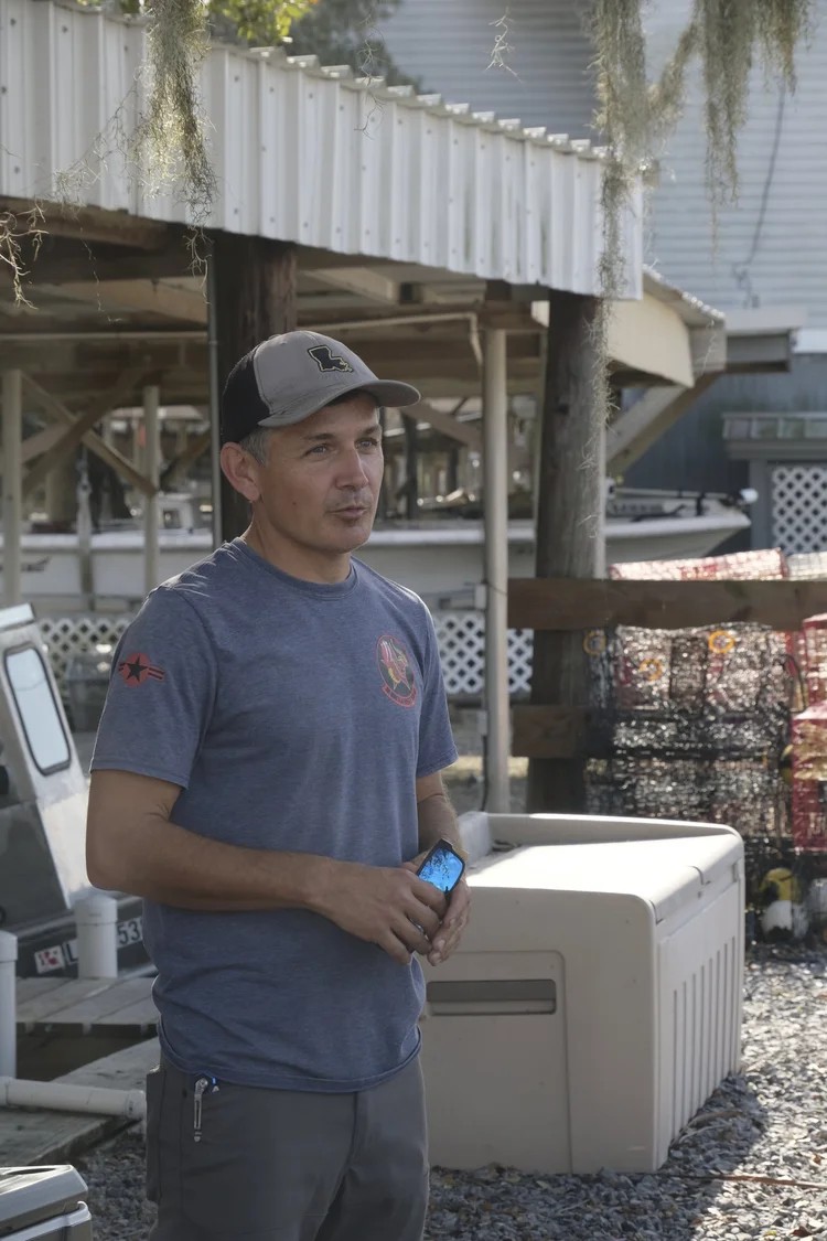 Club member in BFF shirt standing near stacked crab traps at the bayou dock