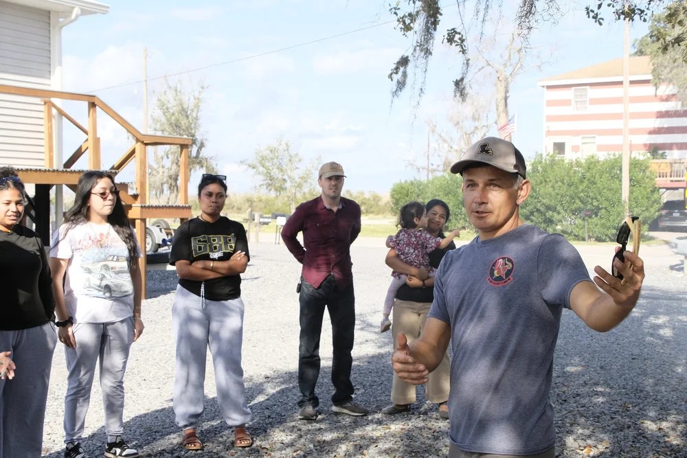 Club leader addressing a group of families outdoors near bayou homes