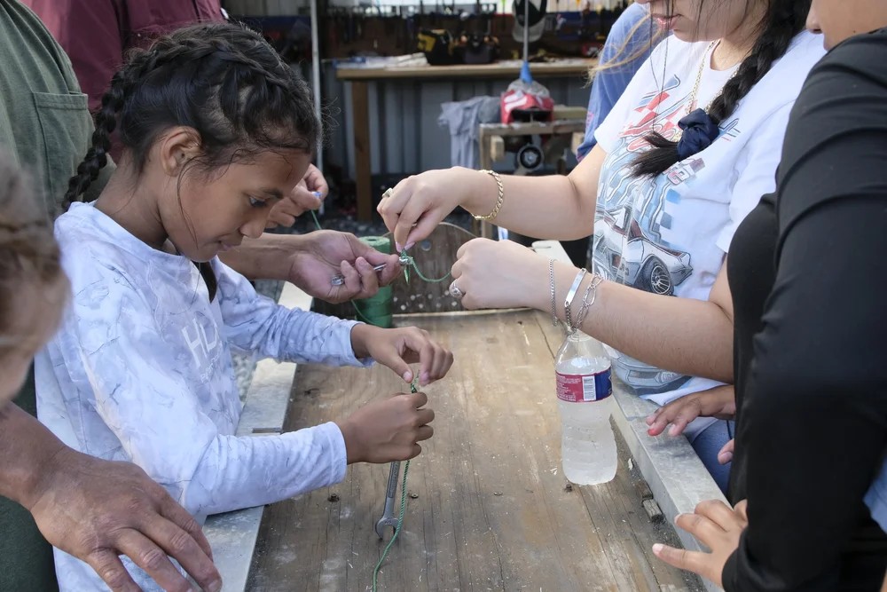 Young girl learning to tie a fishing knot with help from an adult volunteer
