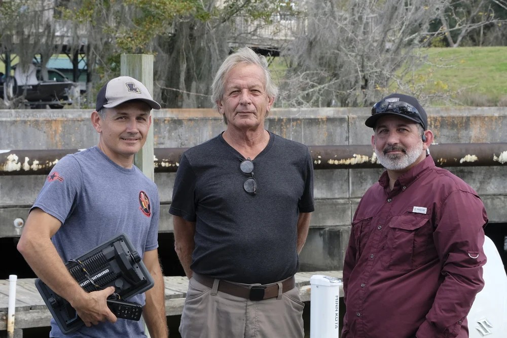 Three men posing at the dock, one holding a Humminbird fish finder